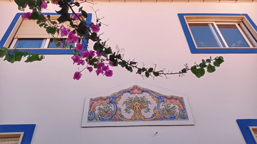Dům s okny s modrým lemováním, mozaika z kachlíků a větvička s růžovými květy