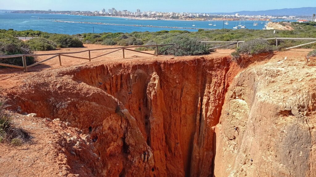 algar, díra v zemi způsobená erozí v pískovcové skále a výhled na oceán a město