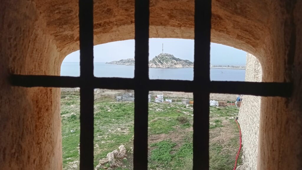 výhled z pevnosti se zamřížovaným oknem na moře a ostrov