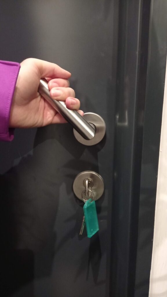 ruka držící kliku u dveří a zámek s klíči