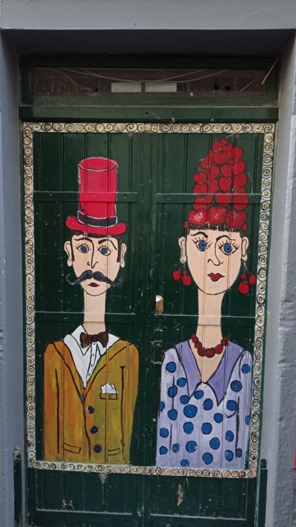 Malované dveře s mužem s červeným kloboukem a ženou s červenými náušnicemi a náhrdelníkem