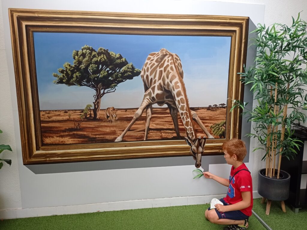 Obraz se stromem a žirafou, kdy žirafa vystrkuje hlavu z obrazu