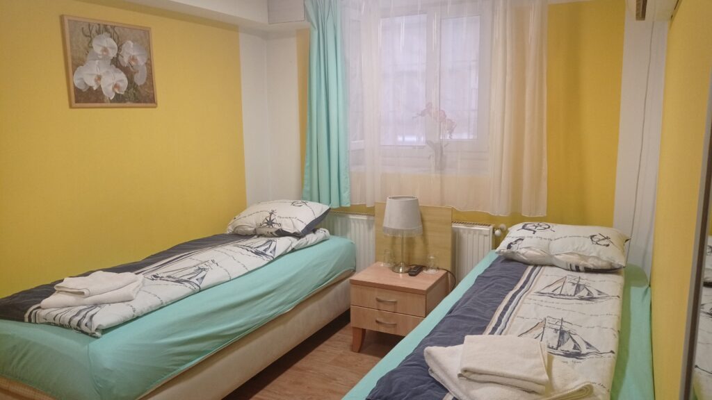 Pokoj se žlutými zdmi a dvě jednolůžkové postele a noční stolek