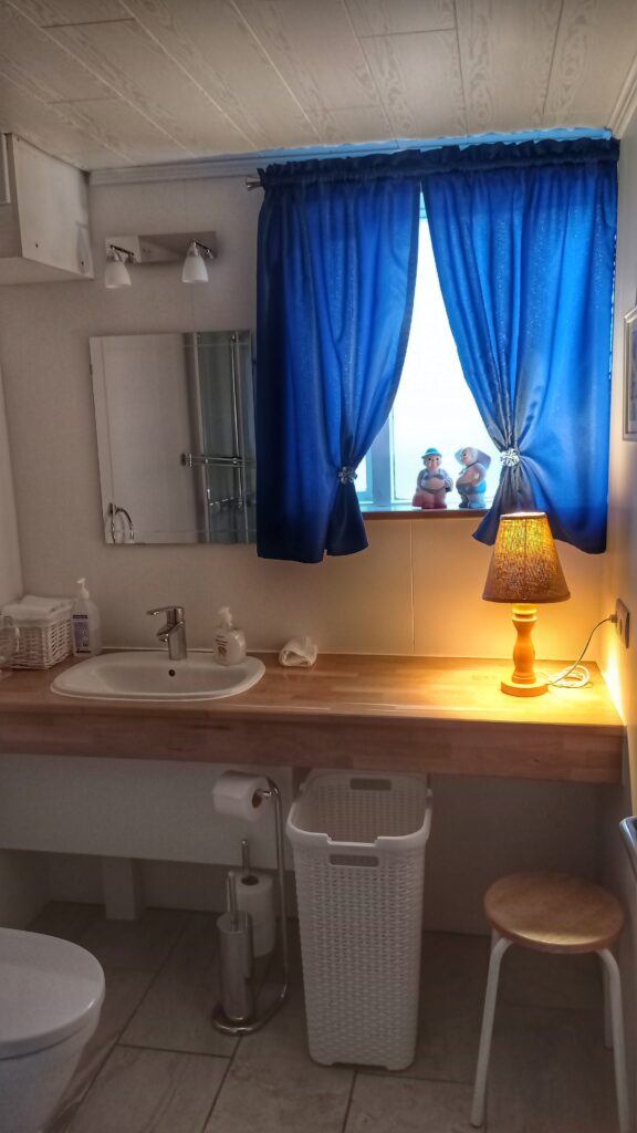 koupelna s oknem a modrými závěsy a umyvadlo nad kterým je zrcadlo