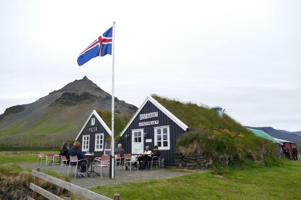 Dva domky s restaurací se střechou porostlou trávou a modročervená vlajka