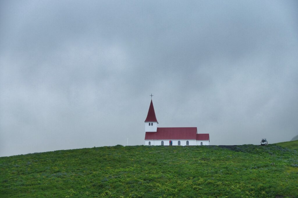 Červenobílý kostelík na kopci s trávou