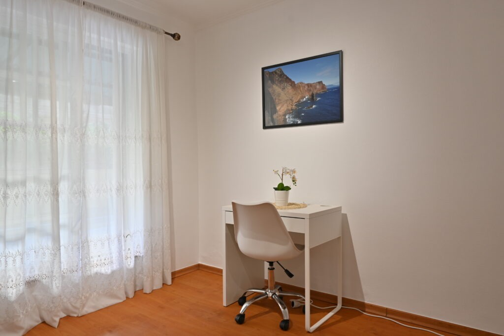 Obývák s oknem se záclonou a malý stůl s židlí
