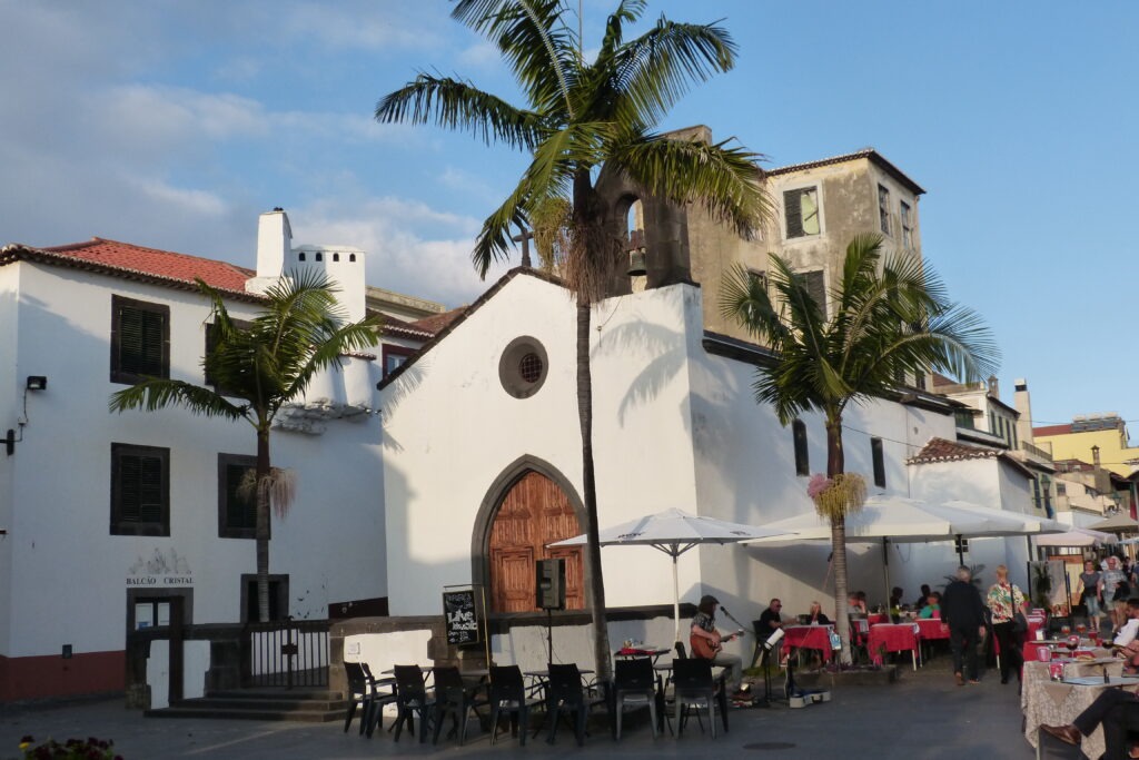 Kostelík u restaurace s venkovním posezením a tři palmy