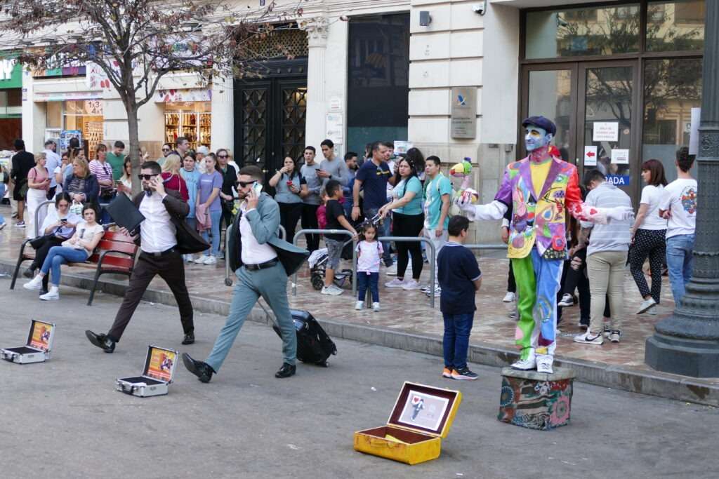 Lidské sochy v ulicích, dva elegantní pánové s kufříkem a jeden klaun v barevném oblečení