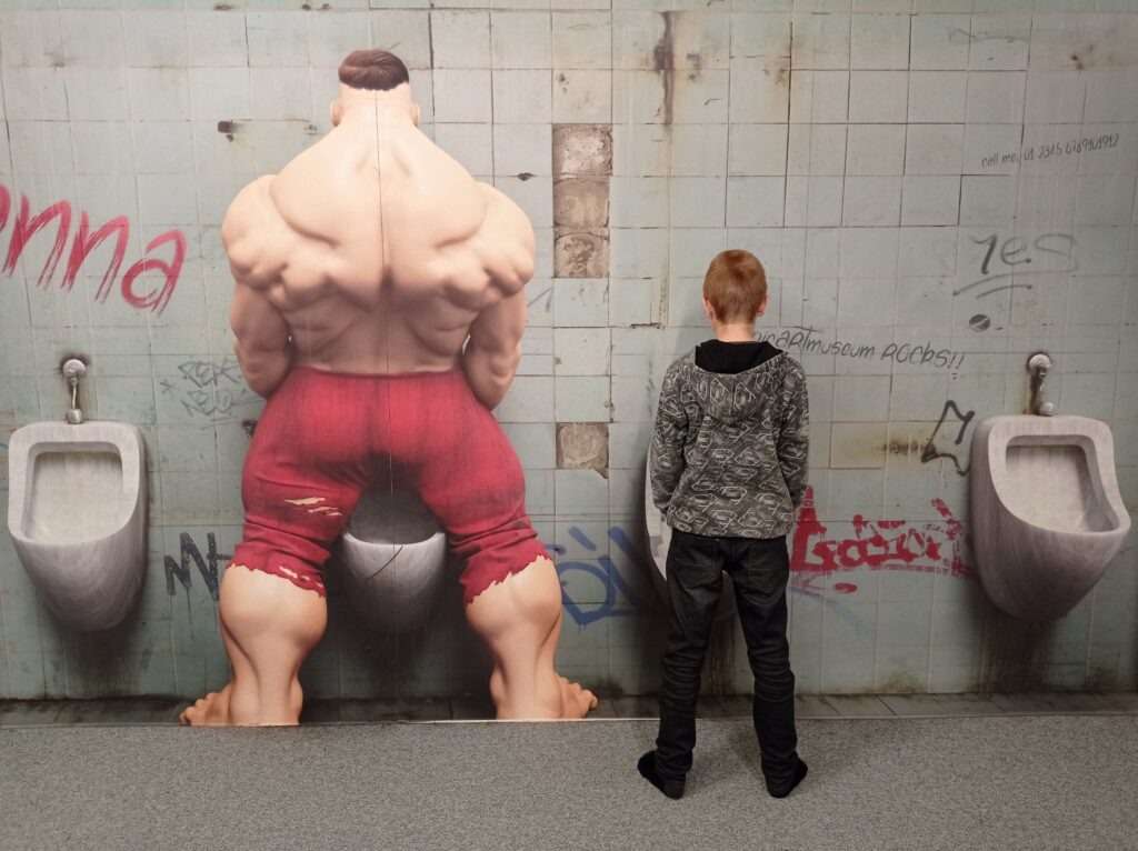 optický efekt v 3D muzeu kde je svalnatý muž a dítě na veřejných záchodech