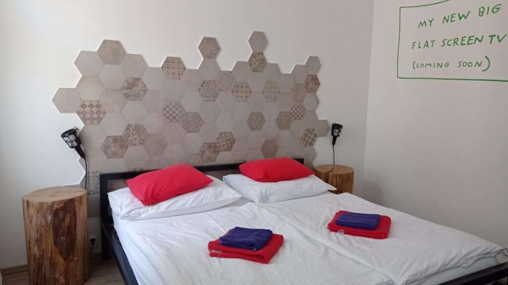 Hotelový pokoj s manželskou postelí, bílým povlečením a červenými polštáři a ručníky