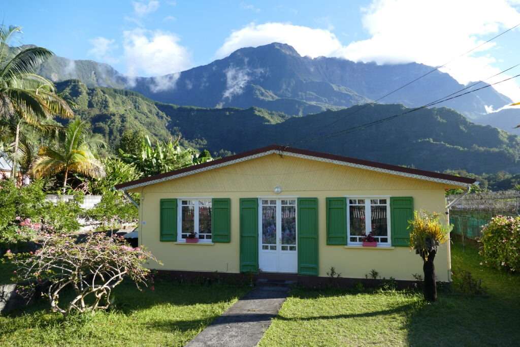 Žlutý rodinný dům se zelenými okenicemi a hory v dálce