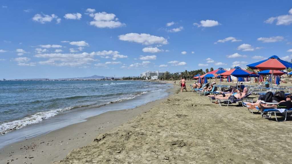 Larnacká pláž s lidmi, slunečníky a letní atmosférou.